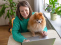 Une femme en train d'utiliser un ordinateur portable avec son chien sur les genoux.